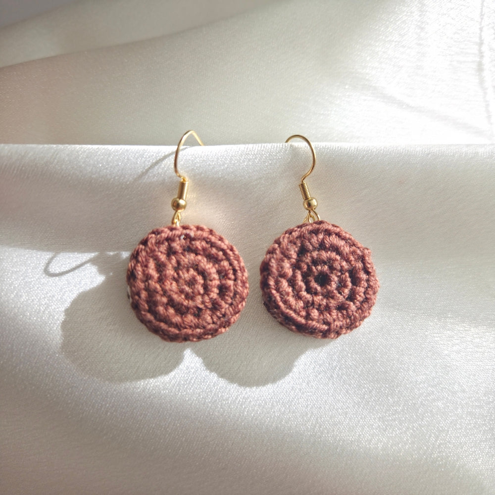 Crocheted chocolate cookie charm earrings on a white fabric background