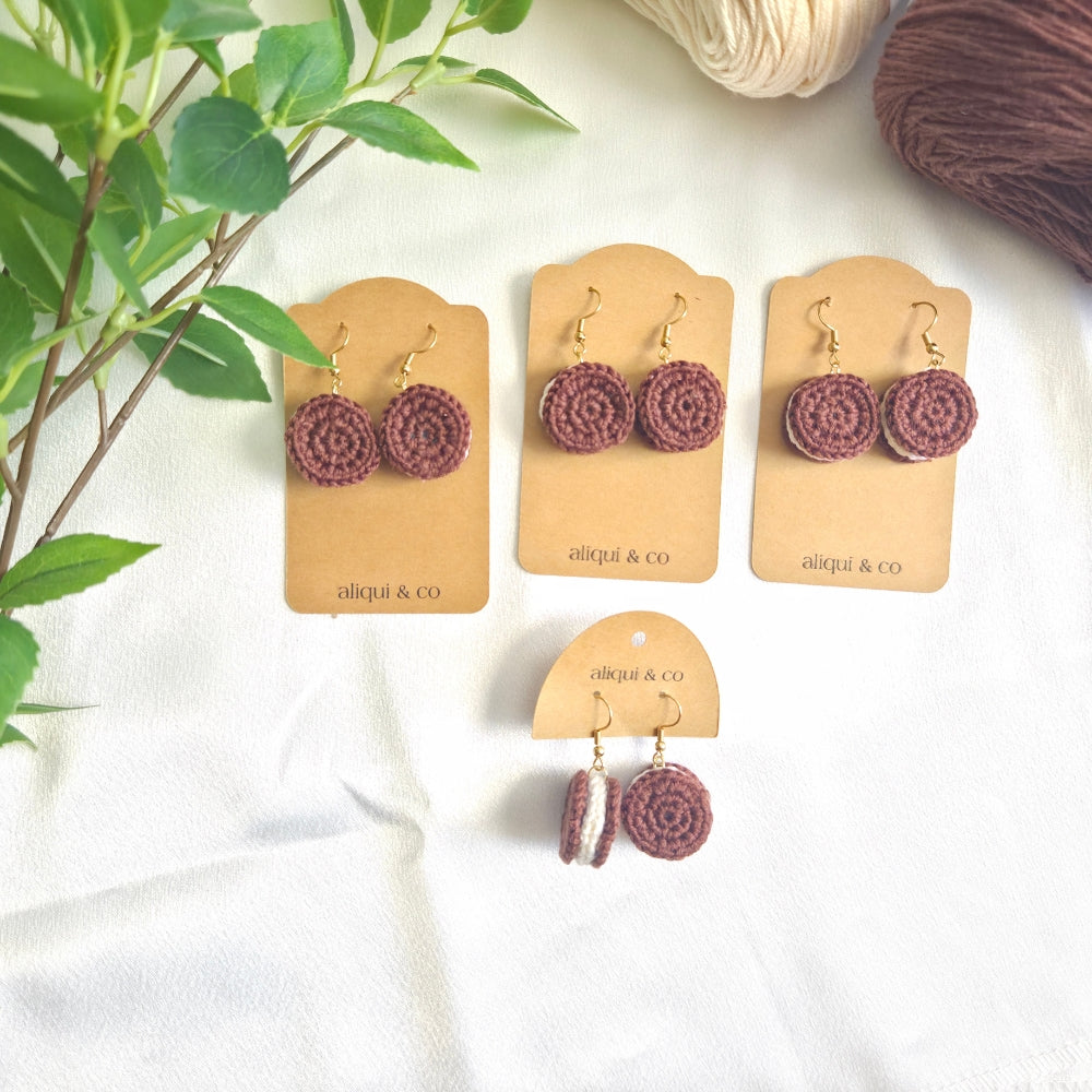 Set of chocolate crochet earrings on 'aliqui & co' cards with yarn and a branch in the background.