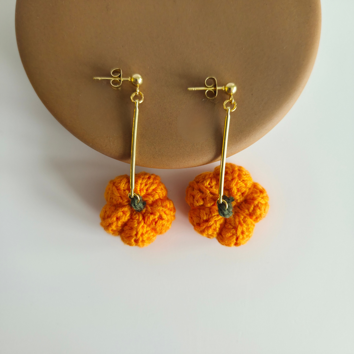Pair of orange crochet pumpkin earrings on a beige stand with a white background