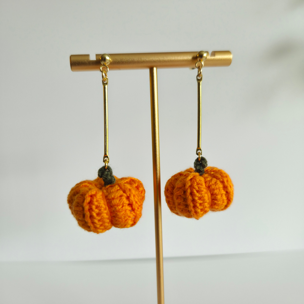 Crocheted pumpkin earrings on a gold earring stand against a white background