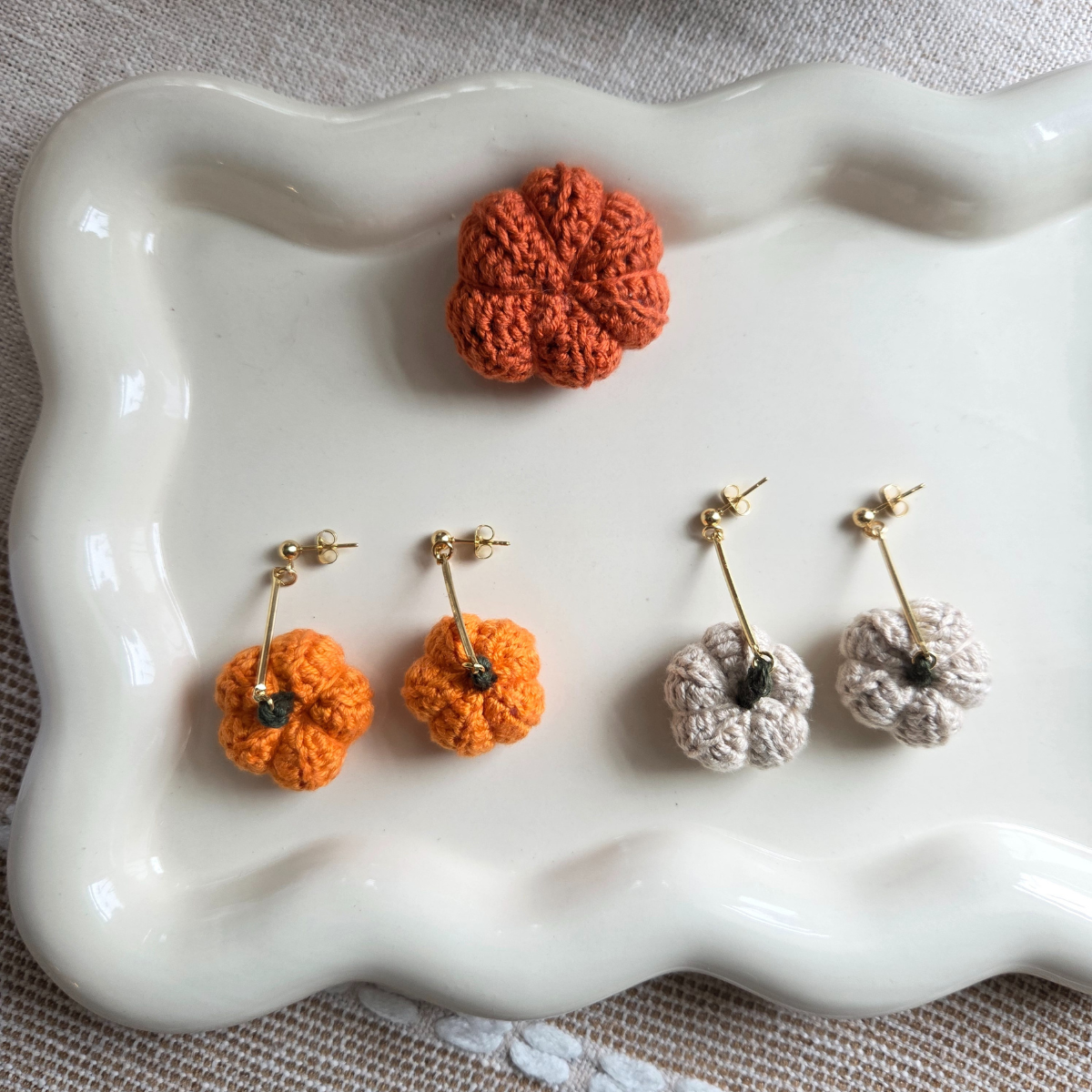 Pair of light tan and orange crochet earrings on a white ceramic dish.