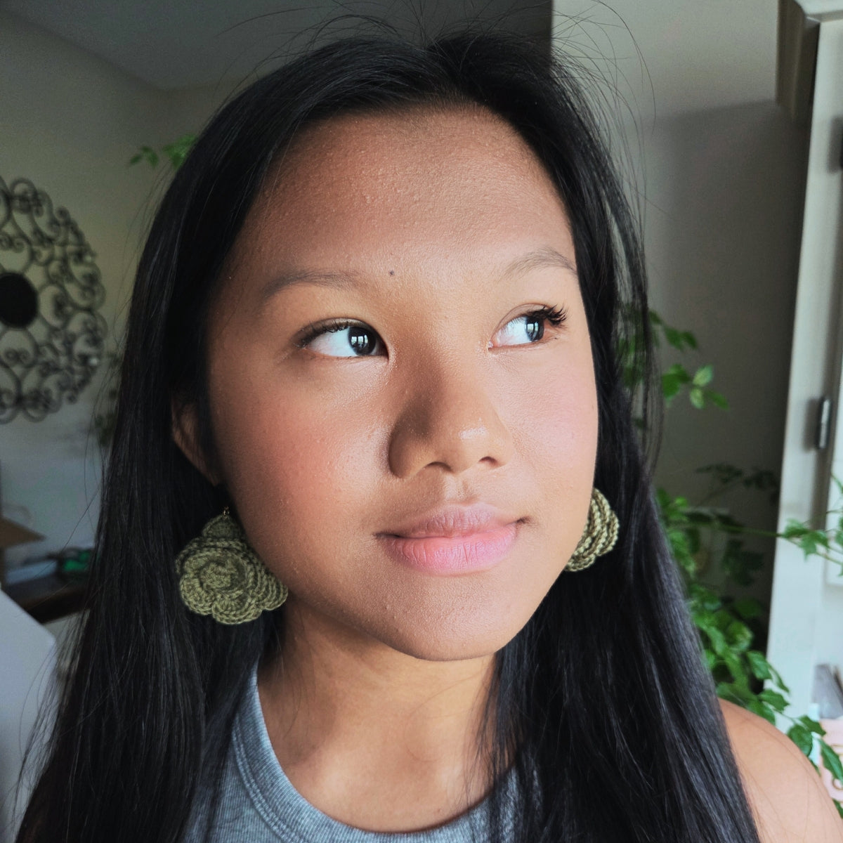 Woman wearing green earrings indoors with plants in the background