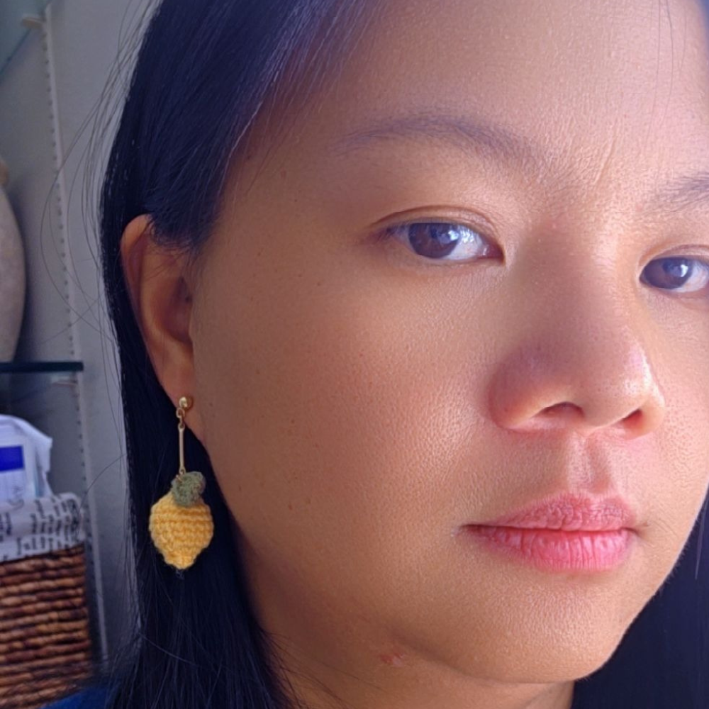 Close-up of a person wearing a yellow crochet earring with a green bead.