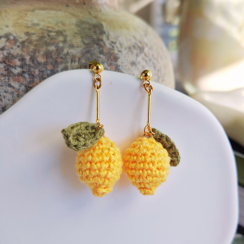 Crocheted lemon earrings on a white surface with a blurred background