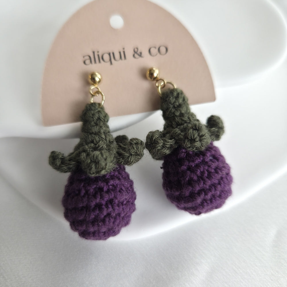 Crocheted earrings with green leaves and purple bases on a 'aliqui & co' branded card.