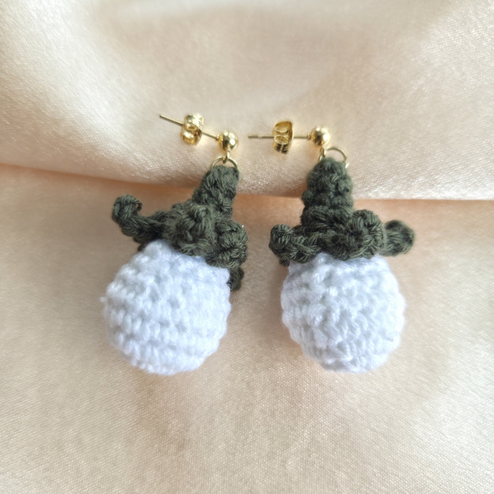 Crocheted white earrings and green stem details on a beige background