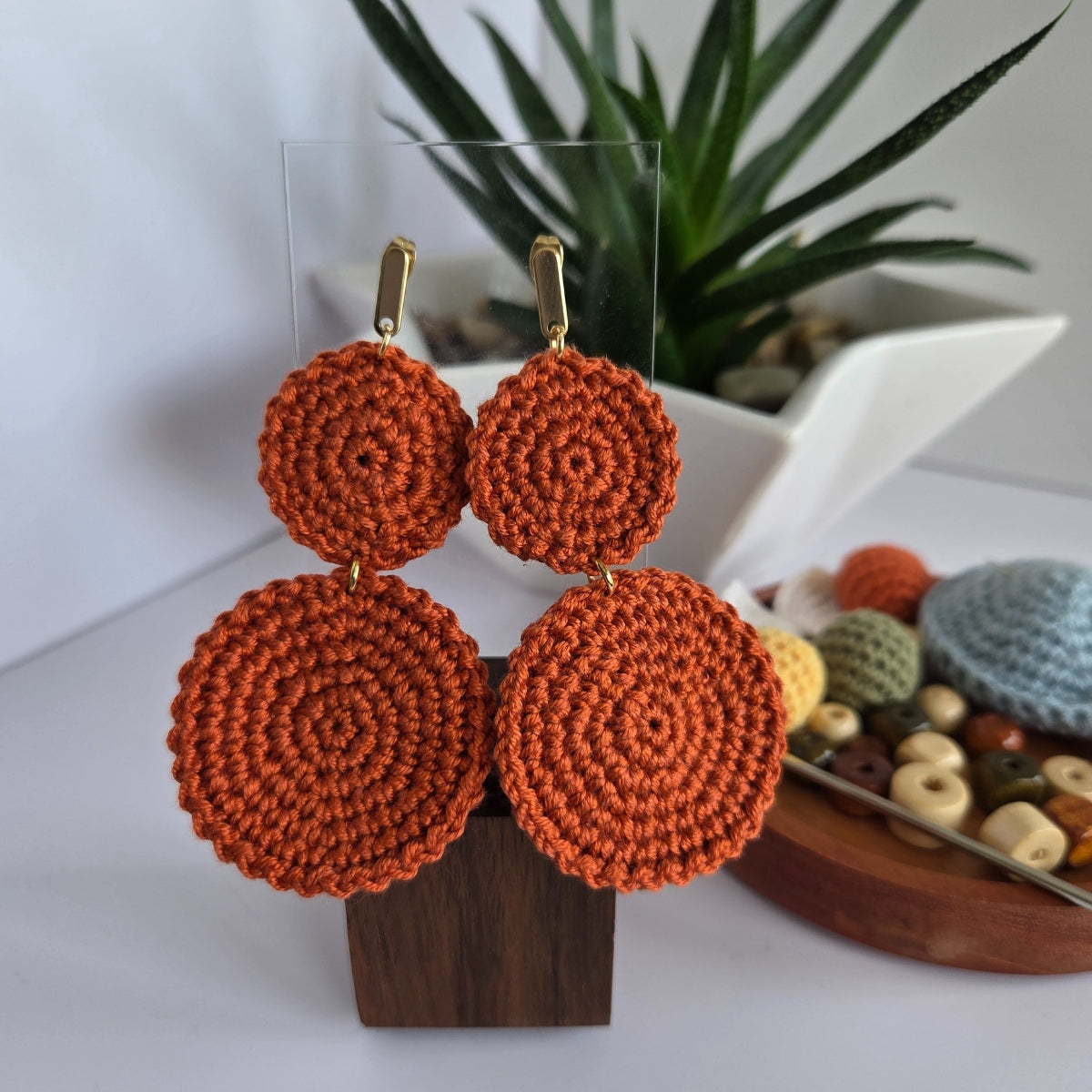 ginger range crochet earrings on a wooden stand with a blurred plant and beads in the background