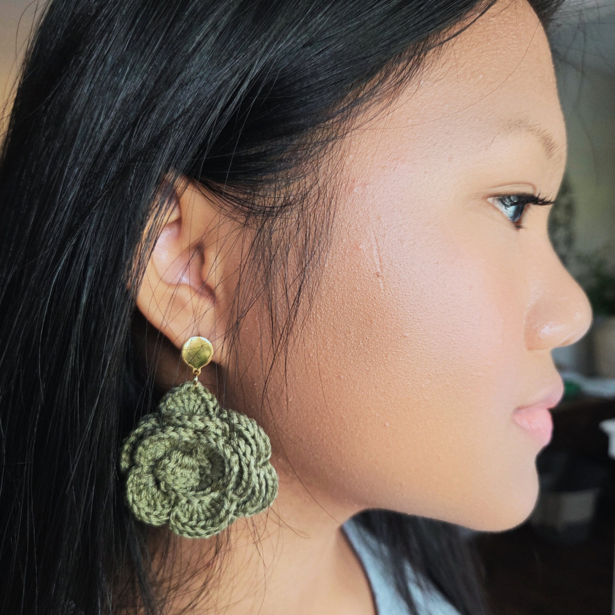 Close-up of a person wearing green rose crochet earrings.