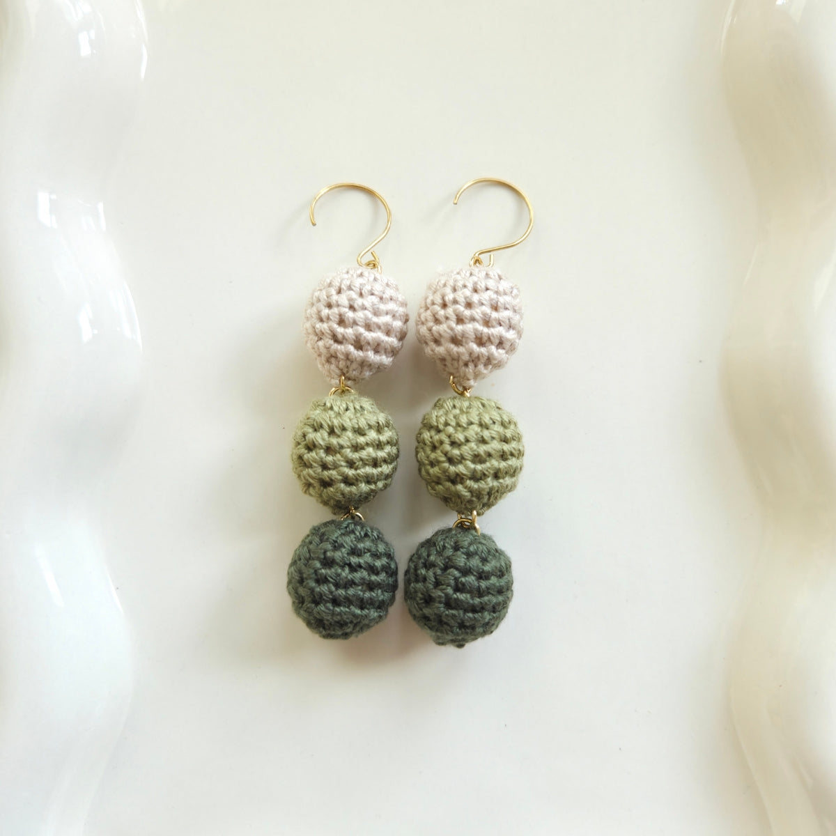 green crocheted ball earrings on a white dish
