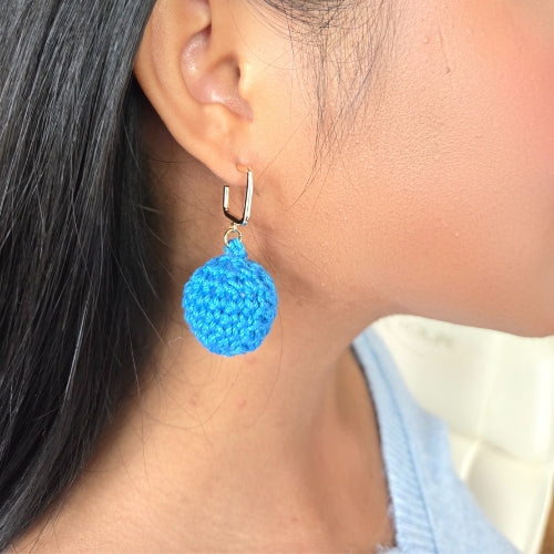 Close-up of a person wearing blue crochet ball earrings on square stud
