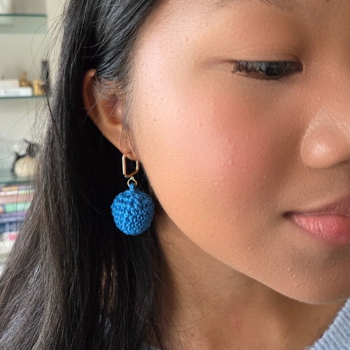 Close-up of a person wearing blue crochet earring with gold studs
