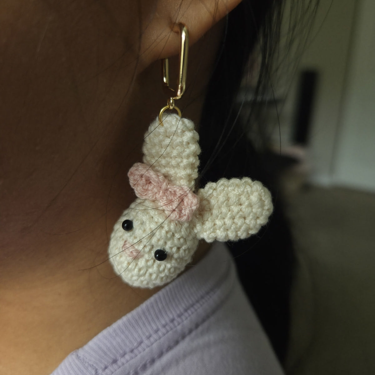 Crocheted rabbit earring gold with a bow worn on an ear.