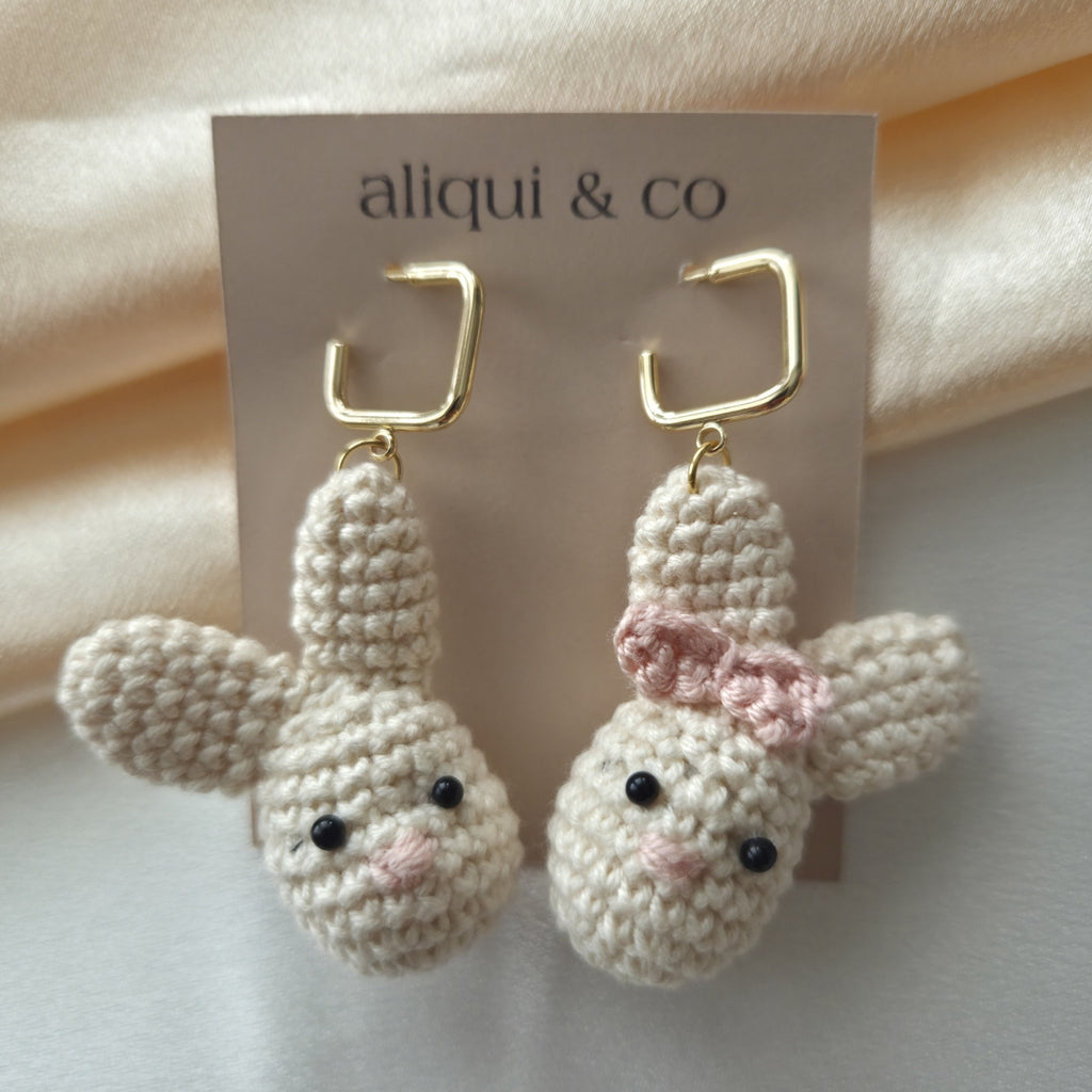 Crocheted bunny earrings with a pink bow on a 'aliqui & co' card.