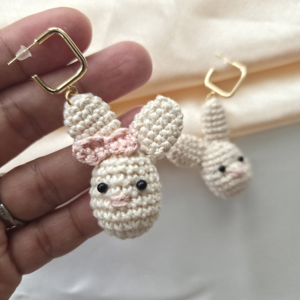 Hand holding a pair of crocheted bunny earrings with gold hooks.