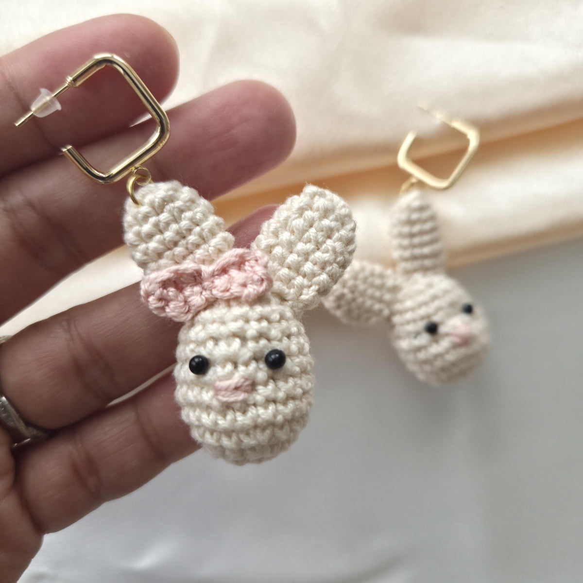 Hand holding a pair of crocheted bunny earrings with gold hooks.