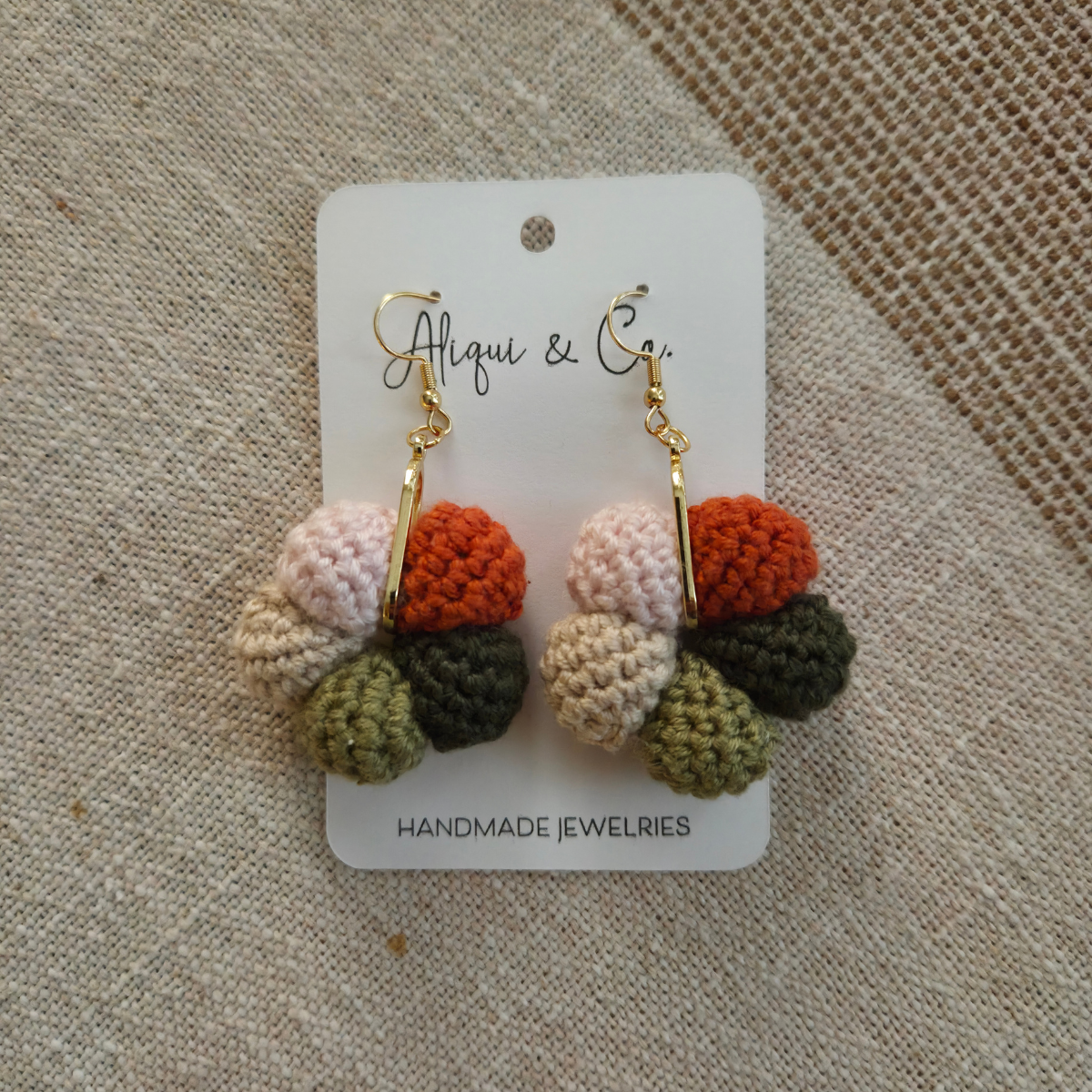 Handmade crocheted earrings on a card with 'Aliqui & Co' branding on a textured fabric background