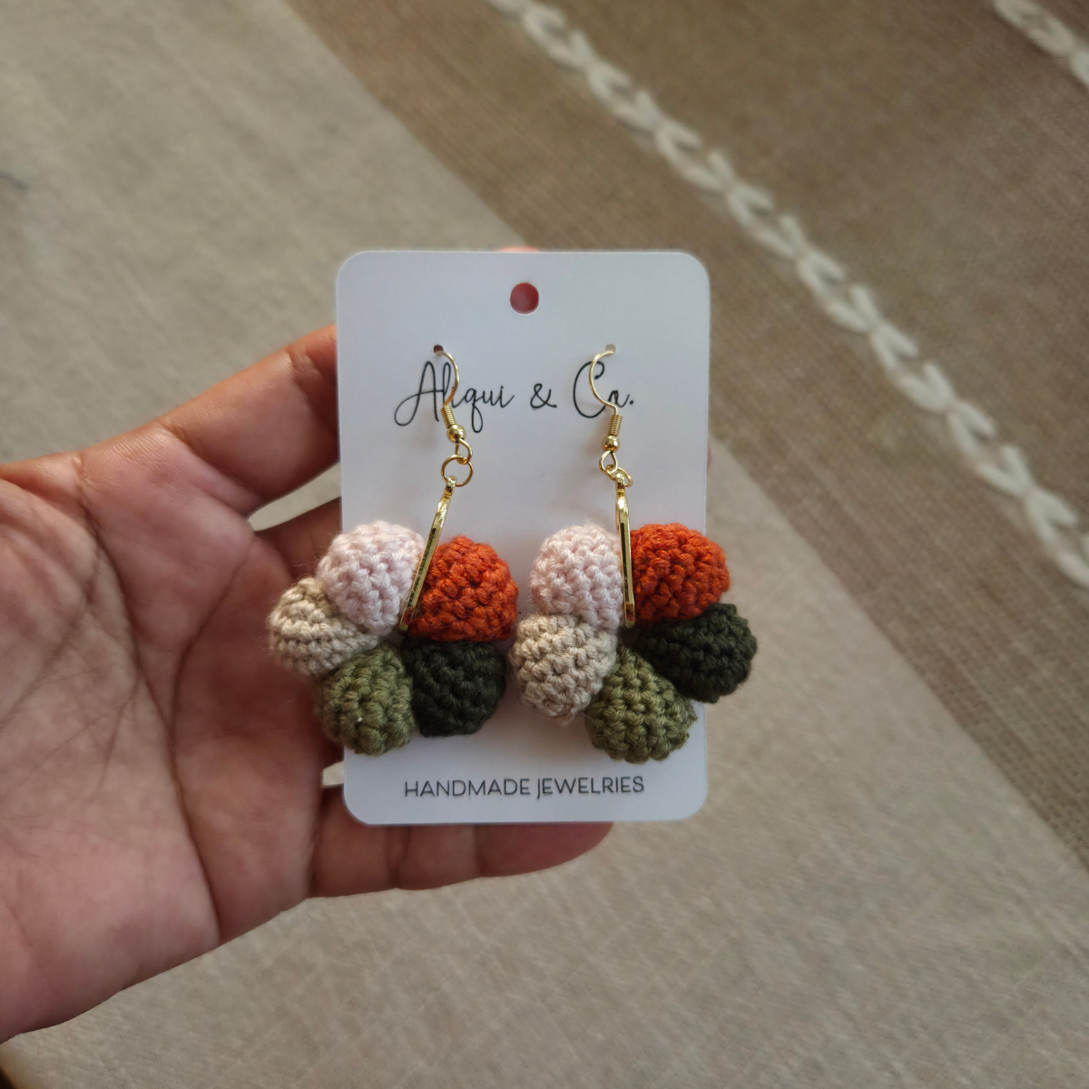 Handmade earrings on a card held by a hand, with a neutral background