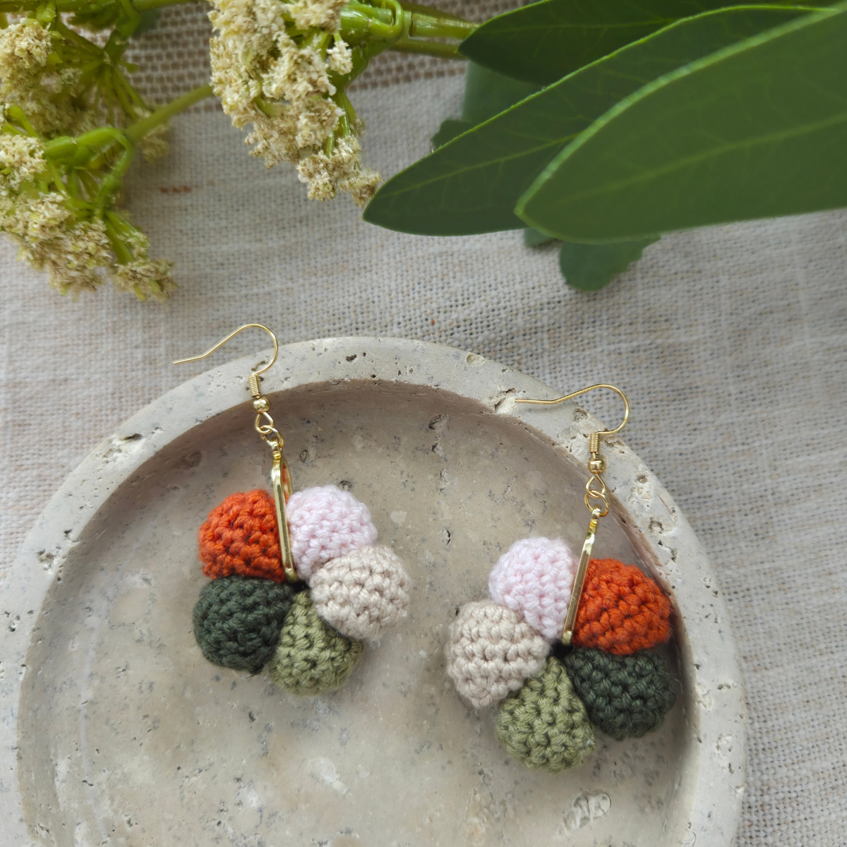Crocheted cluster earrings with colorful berry design on a stone plate with leaves in the background