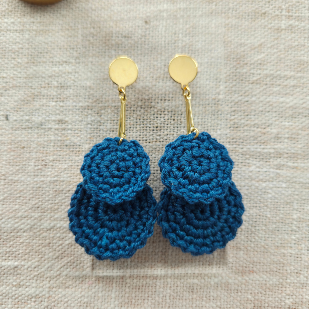 Blue crocheted earrings with gold hooks on a beige fabric background