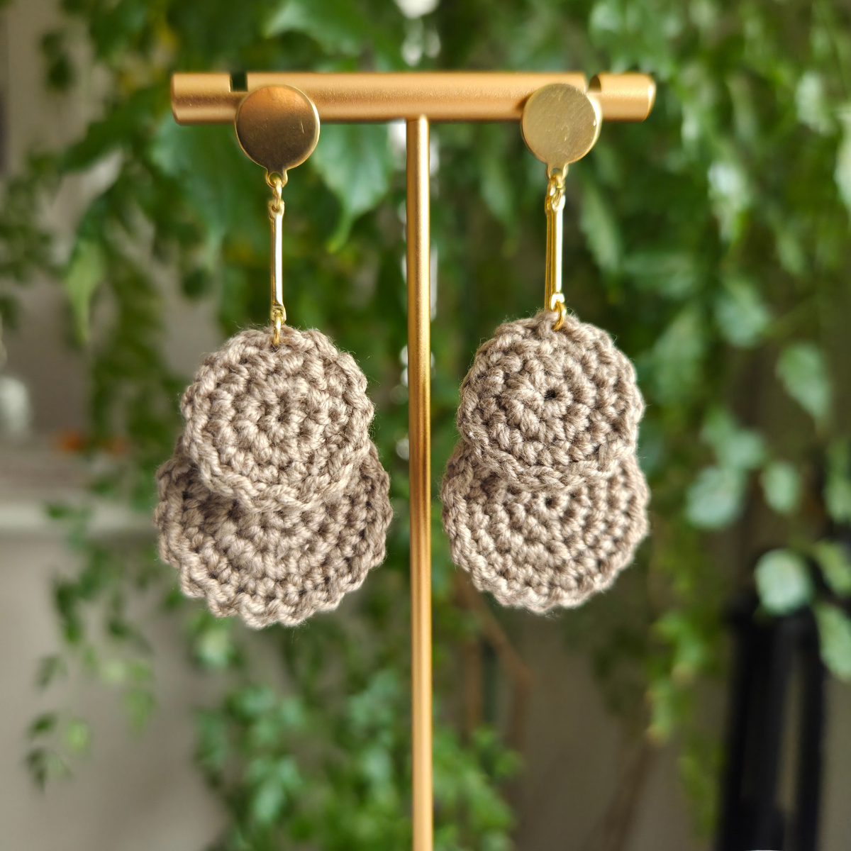 Pair of oak crochet earrings on a gold earring stand with a blurred green plant background