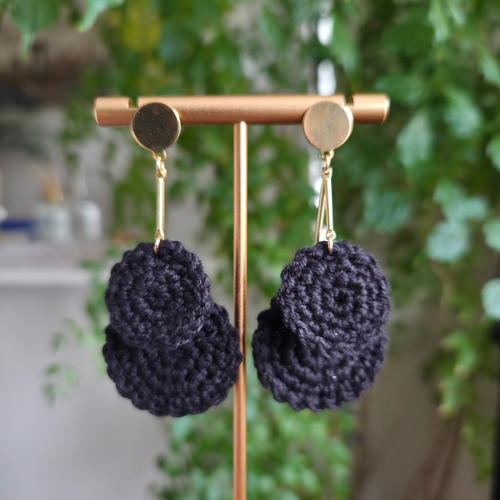 Pair of dark blue crochet earrings on a gold earring stand with a blurred green background