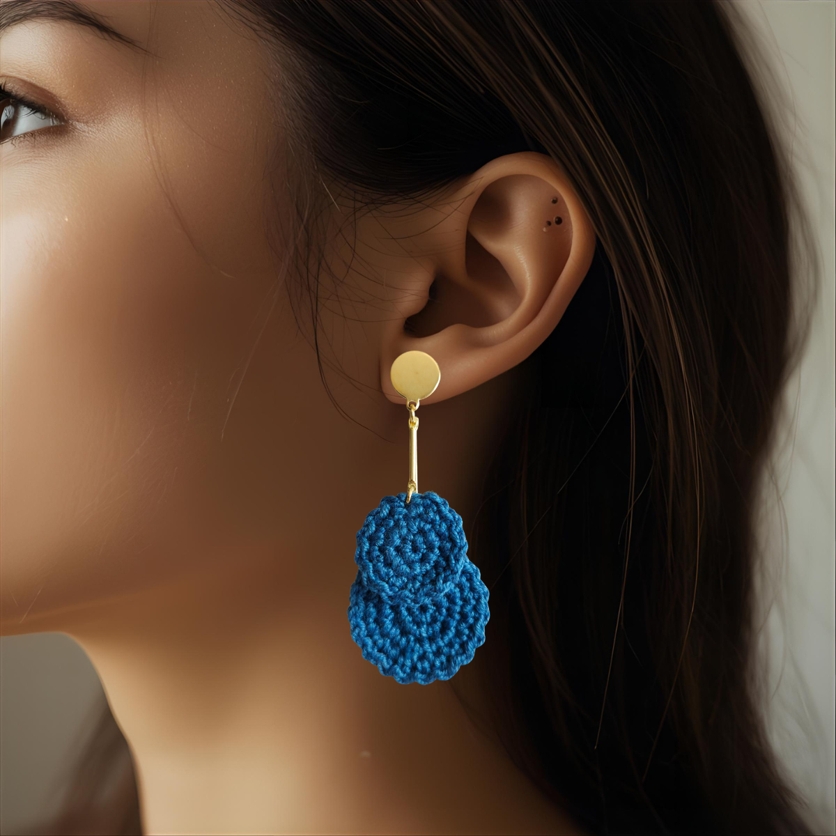 Close-up of a woman wearing blue bohemian crocheted drop earrings with gold studs.