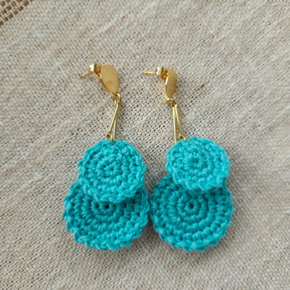 Mint crocheted earrings with gold hooks on a beige fabric background