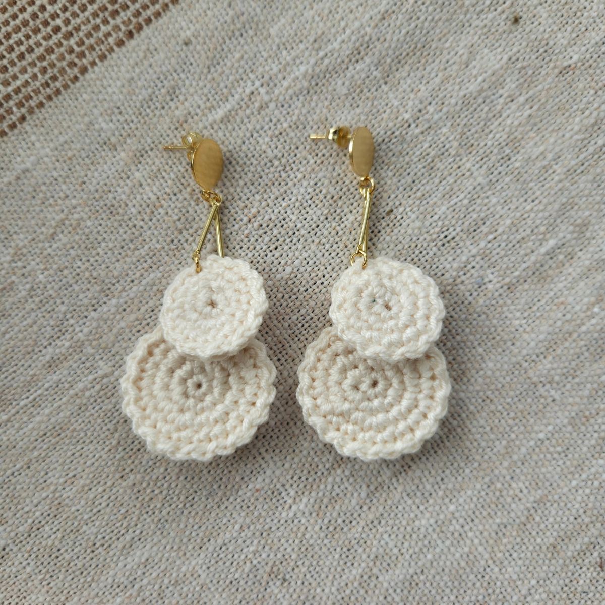 Pair of cream crocheted earrings on a textured fabric background