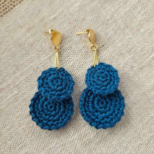 Dark teal crochet earrings with gold hooks on a beige fabric background