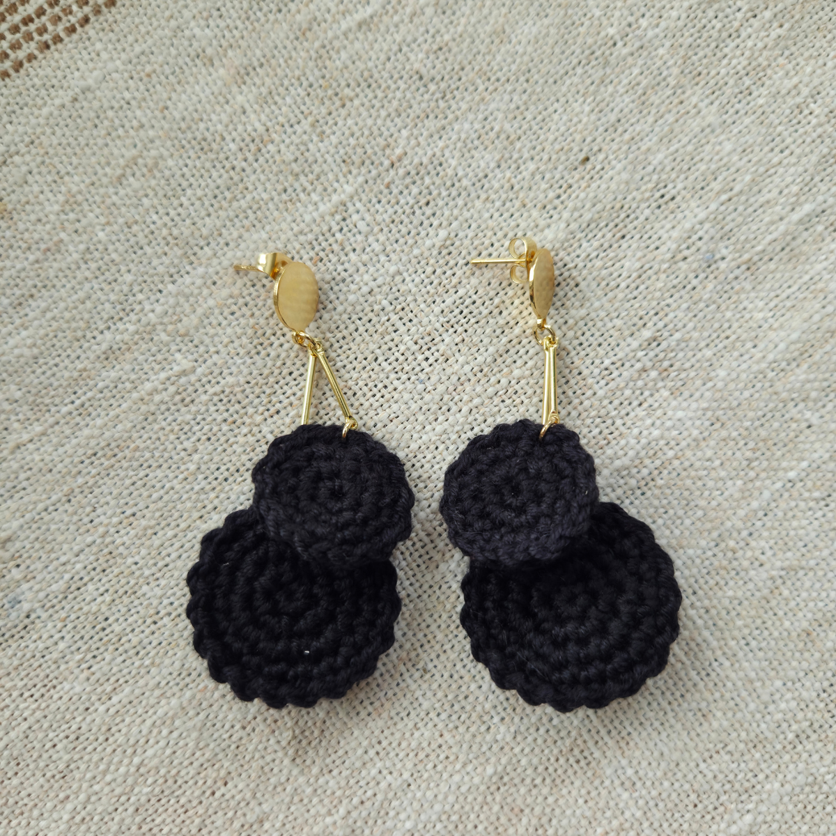 Black crocheted earrings on a beige fabric background