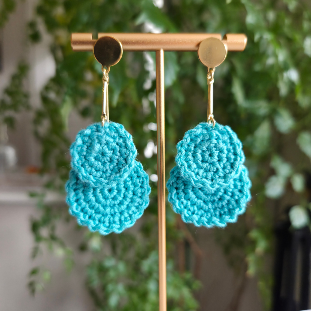 Mint crochet earrings on a gold earring stand with a blurred green plant background