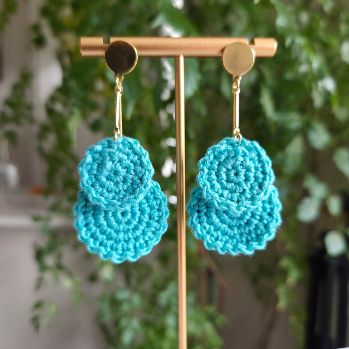 Mint crochet earrings on a gold earring stand with a blurred green plant background