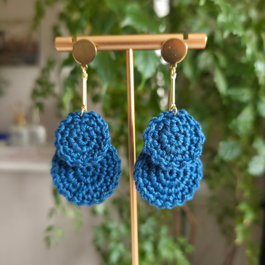 Dark teal crochet earring hanging on a golden bar on a blurred background