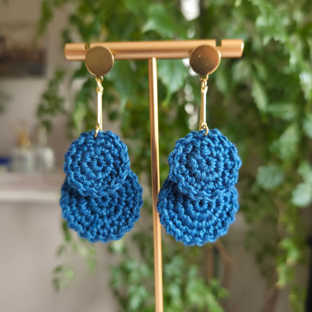 Dark teal crochet earring hanging on a golden bar on a blurred background