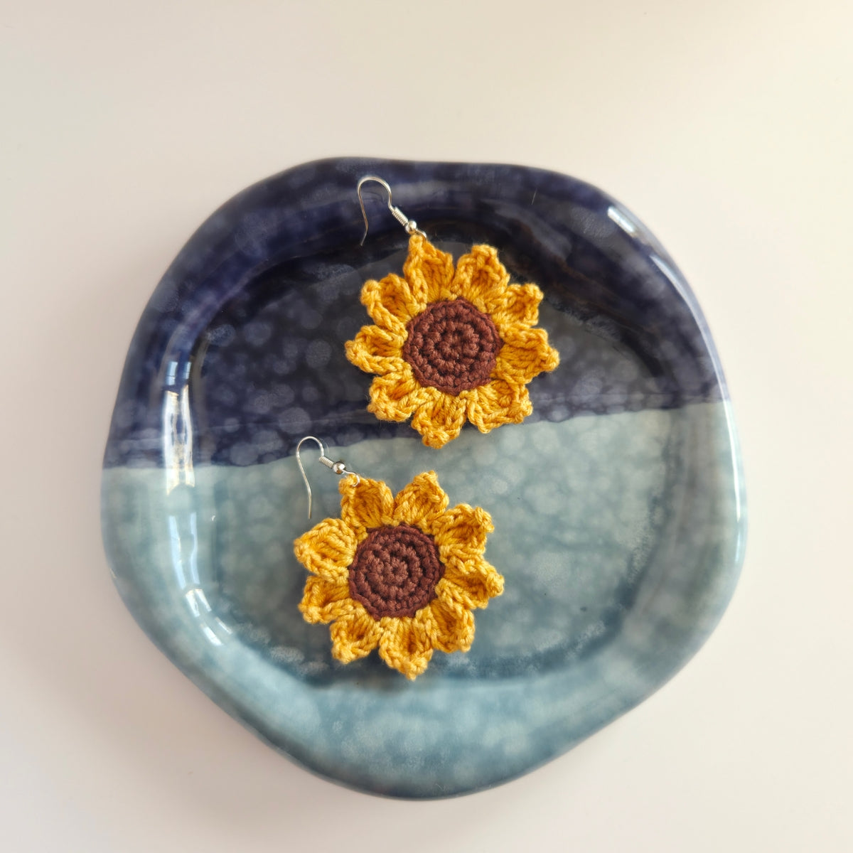 Sunflower-shaped earrings on a blue ceramic dish