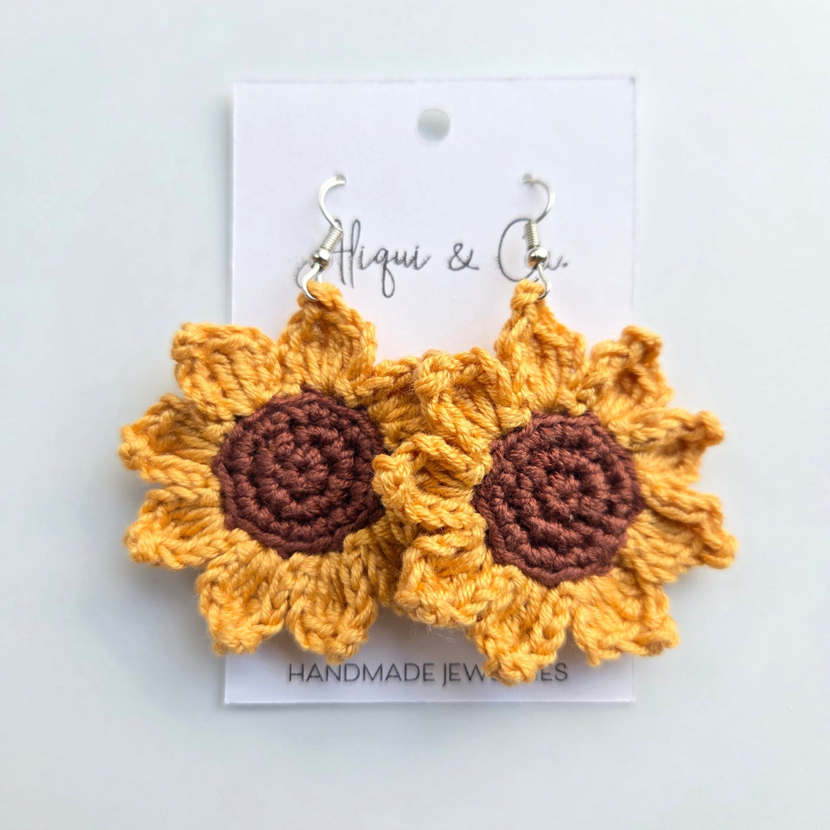 Crocheted sunflower earrings on a white card with 'Aliqui & Co' branding.