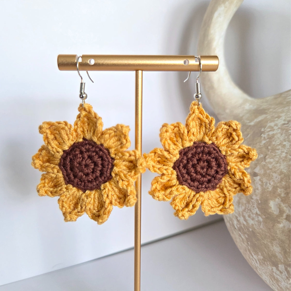 Handmade crocheted sunflower earrings on a gold stand with a neutral background