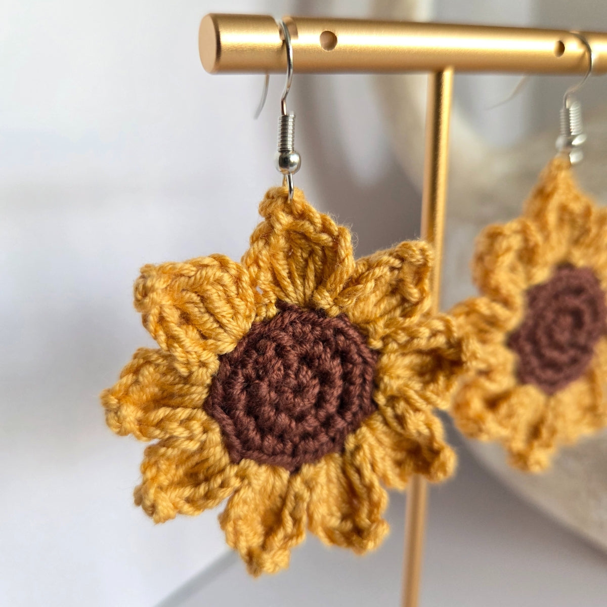 Crocheted sunflower earrings with brown centers on a gold stand.