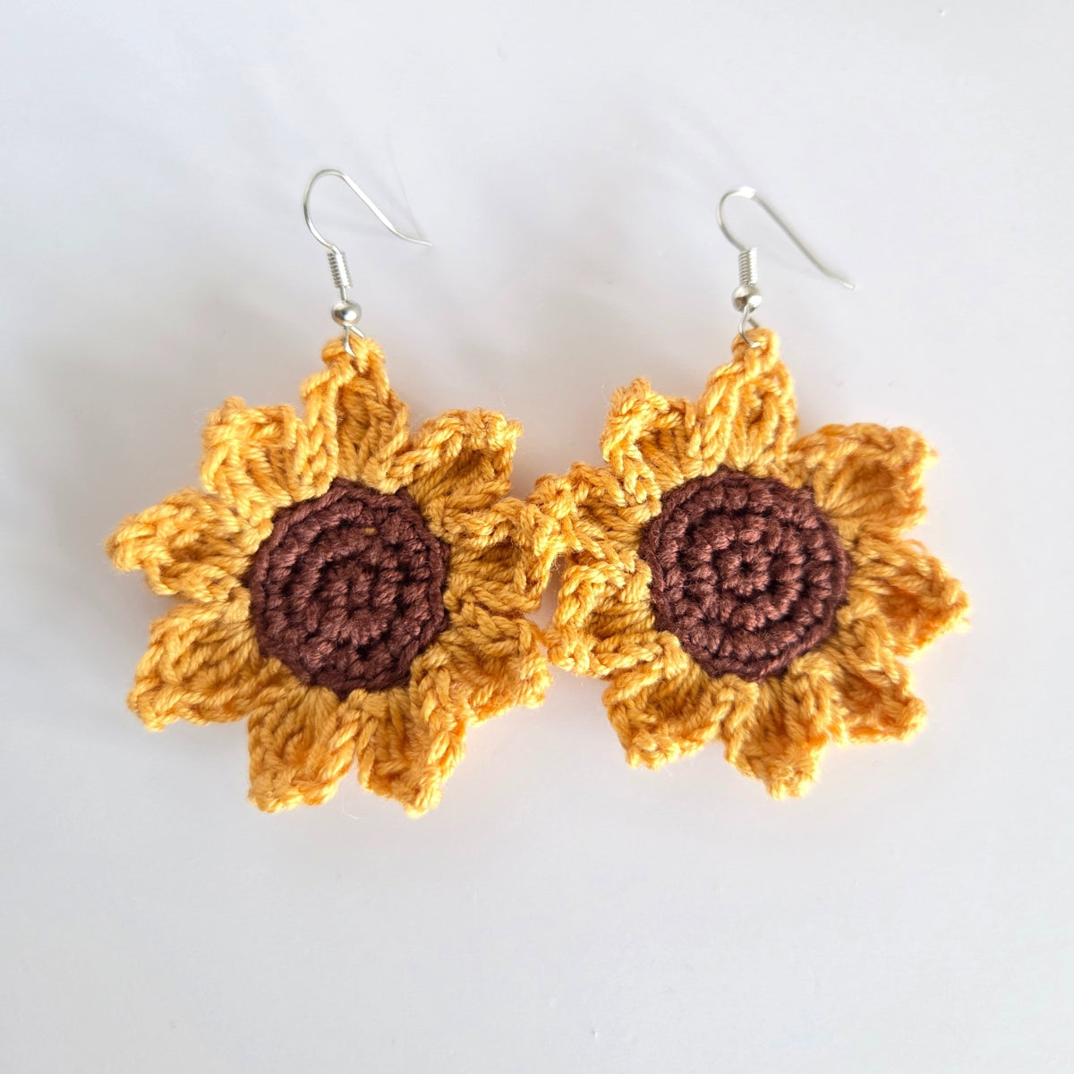 Crocheted sunflower earrings with yellow petals and brown centers on a white background