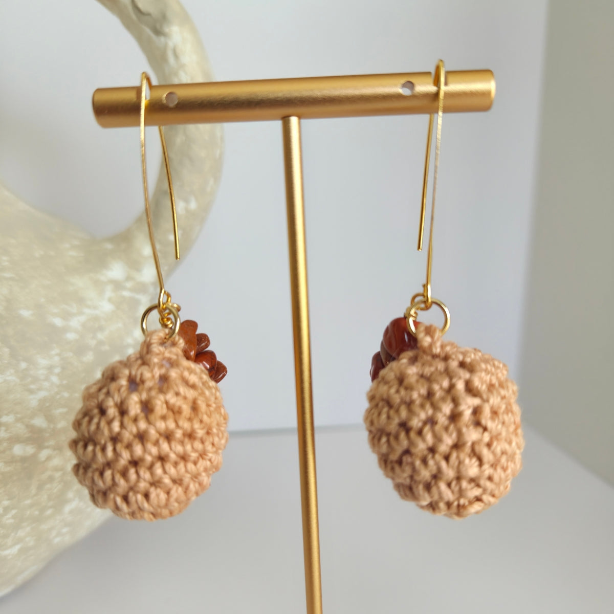 Pair of light brown textured earrings with brown beads on a gold earring stand against a white background.