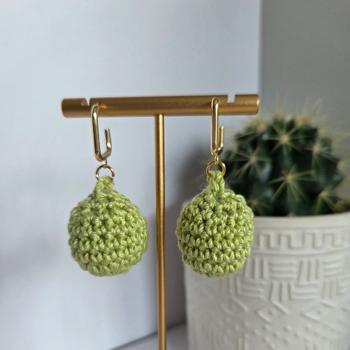 Lime green crocheted earrings on a gold stand with a cactus plant in the background.