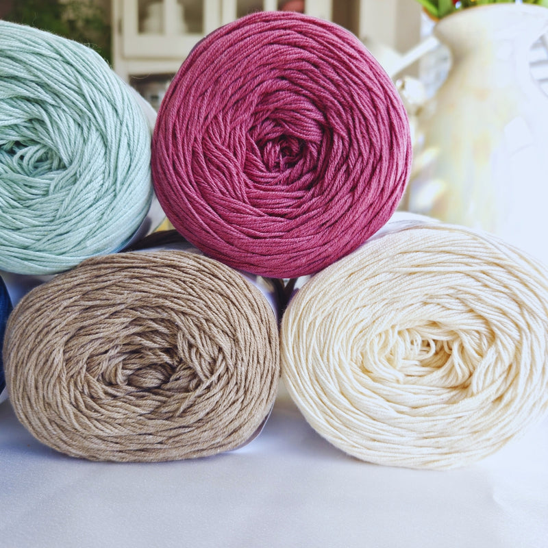 Four skeins of neutral yarn in different colors on a light surface.
