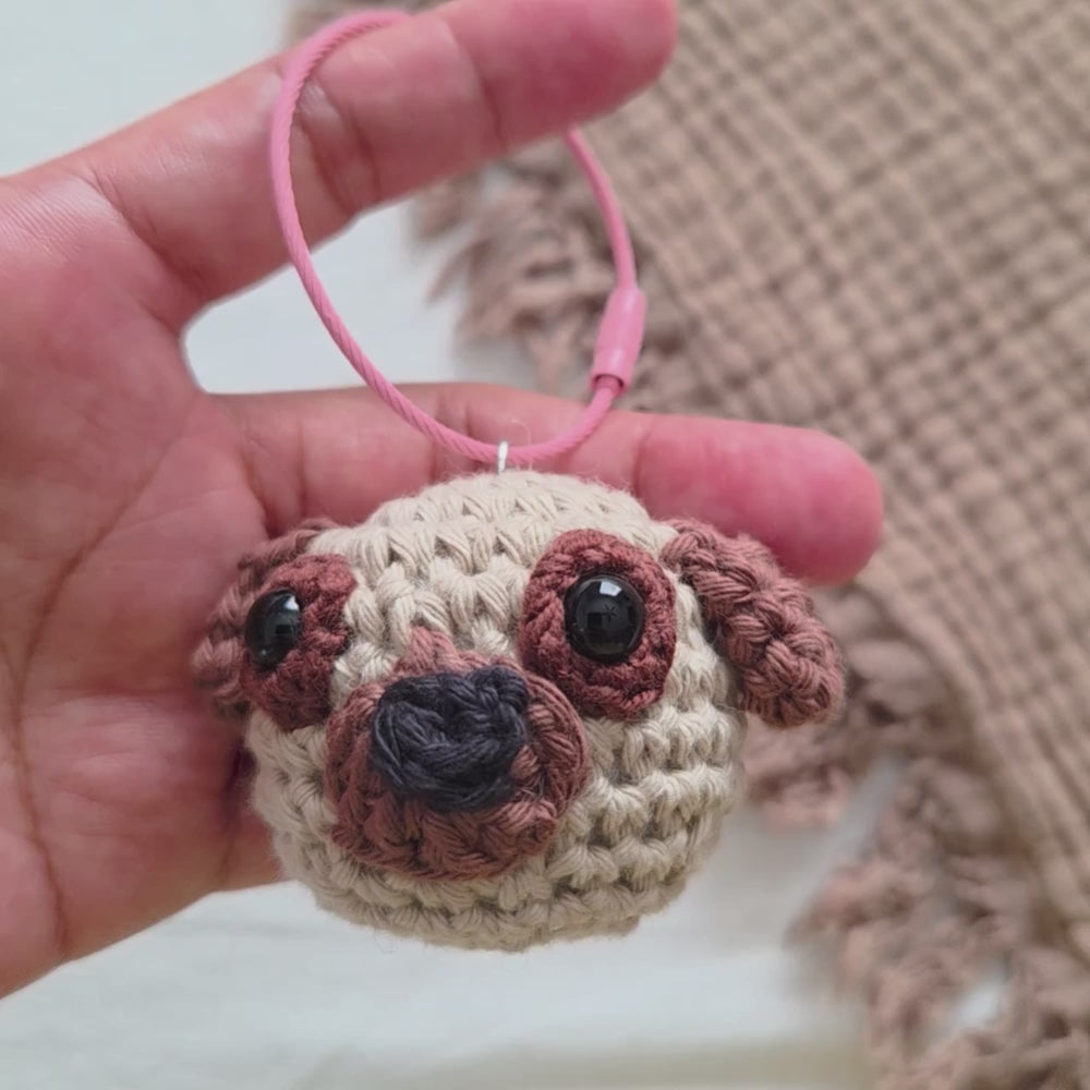 video of a  hand holding a wire keyring of a cute crochet pug dog amigurumi keychain or bag charm