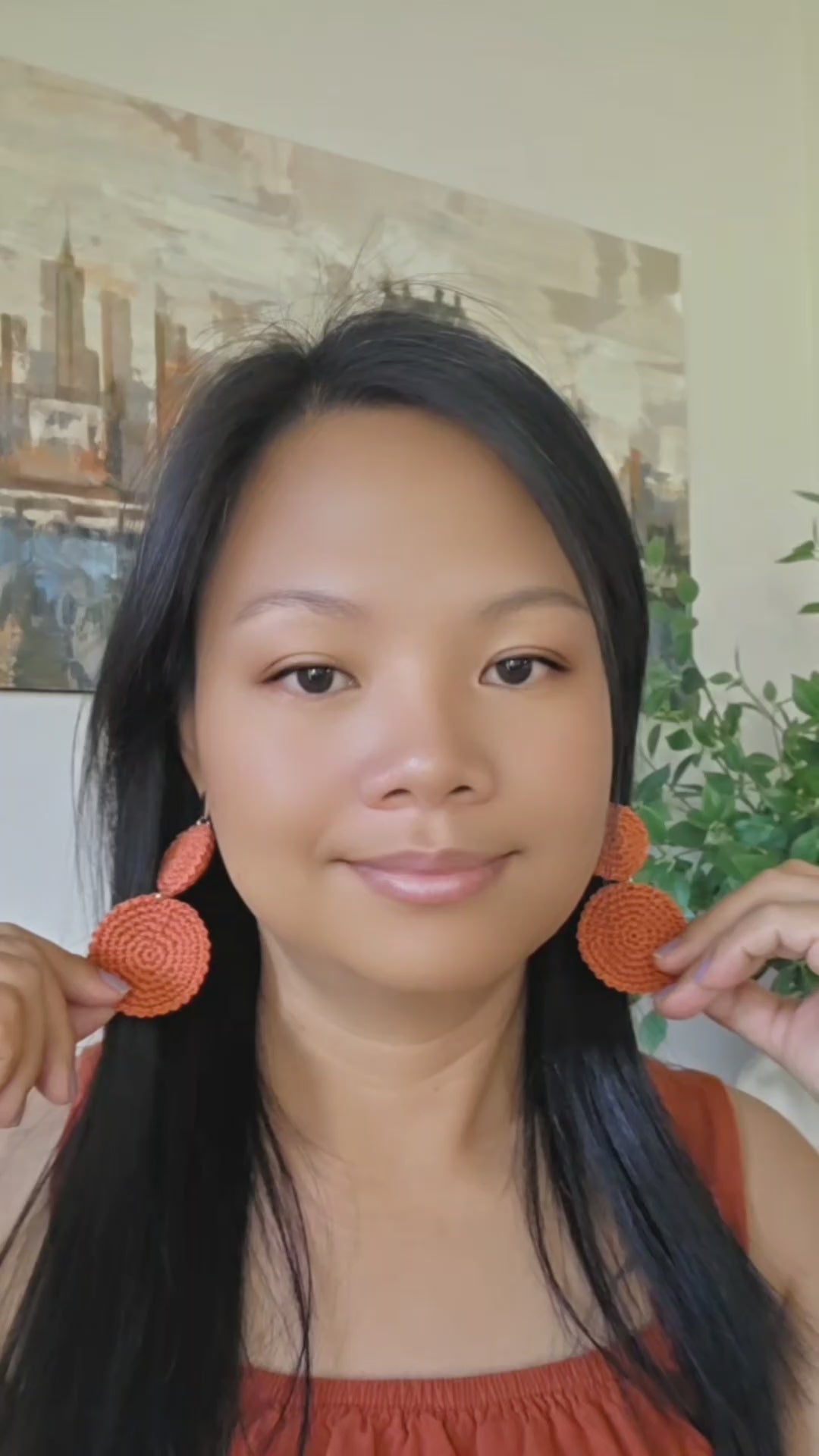 woman wearing an orange crochet boho earrings in a painting and a green plant background