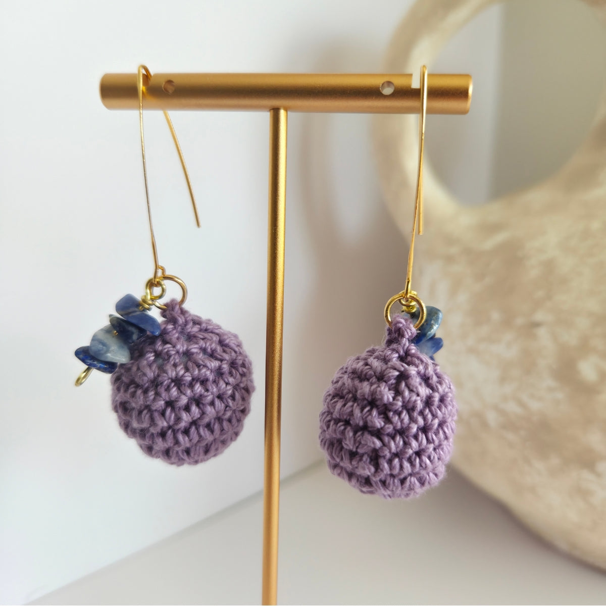 Purple crocheted earrings with bluish purple beads on a gold earring stand.