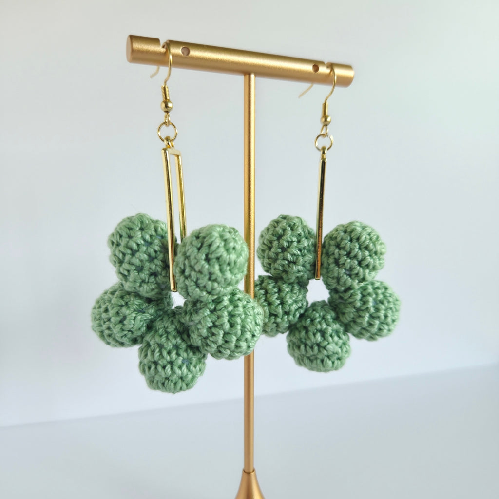sage green crocheted earrings on a gold stand against a light background