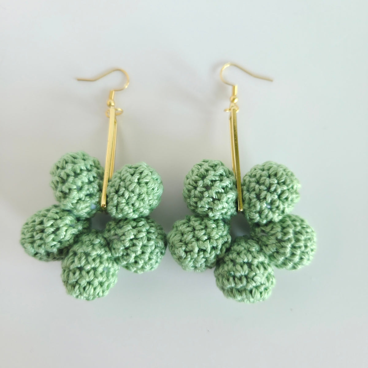Green crocheted earrings with gold hooks on a white background