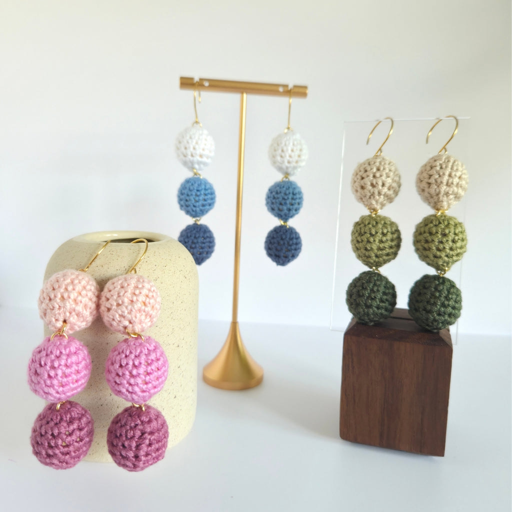Colorful crocheted ball drop earrings on stands against a white background