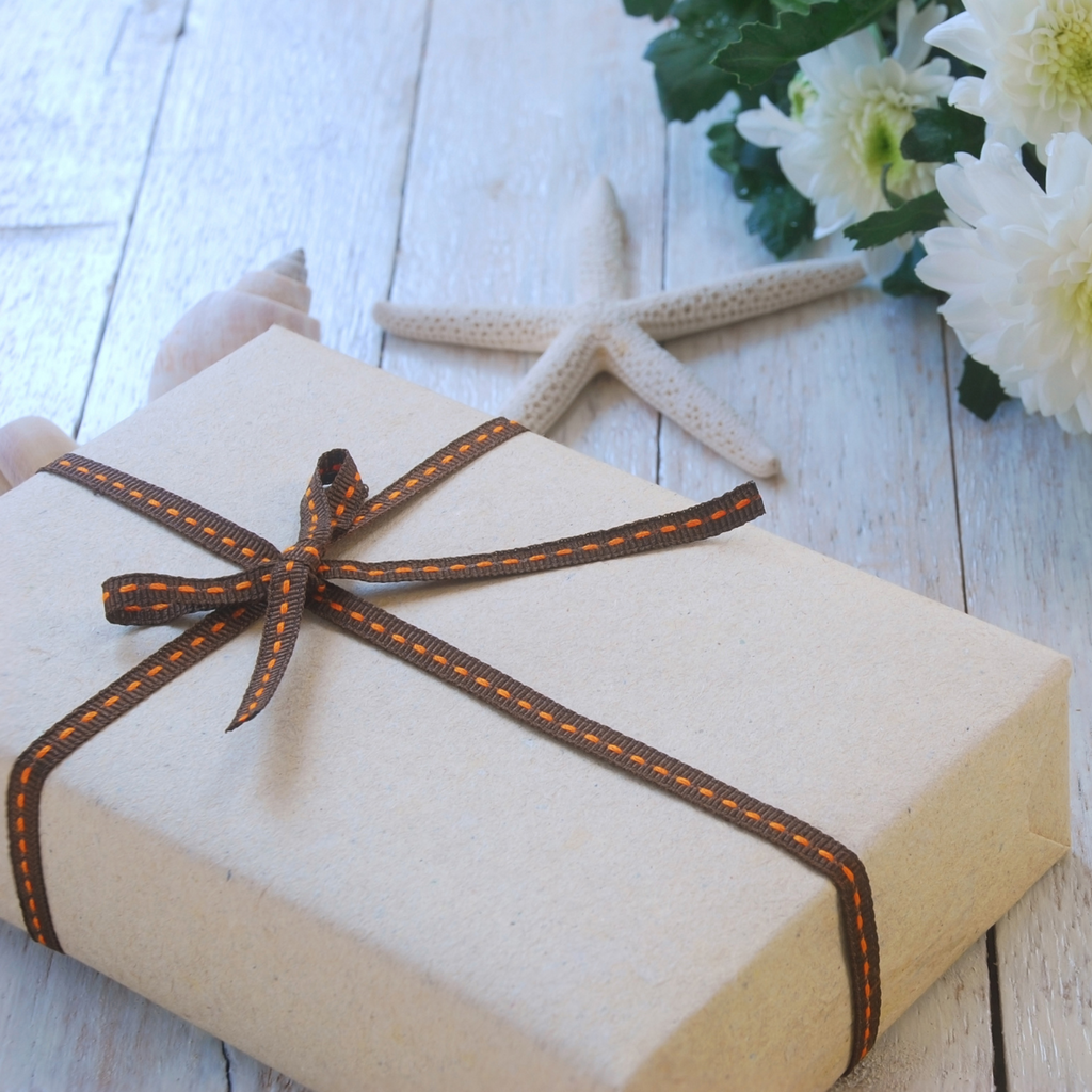 Gift box wrapped with brown ribbon on a wooden surface with flowers and starfish.