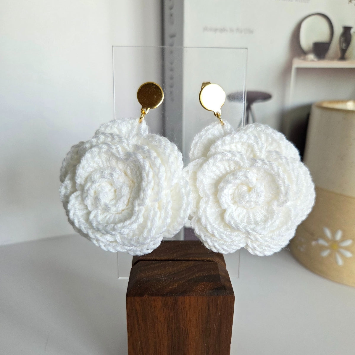 White crocheted earrings on a wooden block with a blurred background